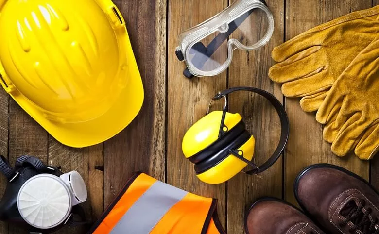 construction vest, safety glasses, ear protection, gloves, and googles laid out on a plank of wood